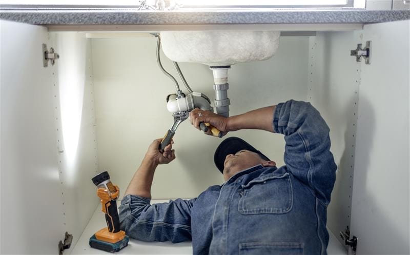 Plumber repairing pipes beneath a bathroom sink in Colton