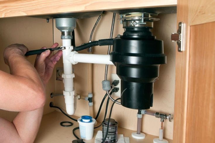 Plumber installing a garbage disposal beneath a kitchen sink in Colton