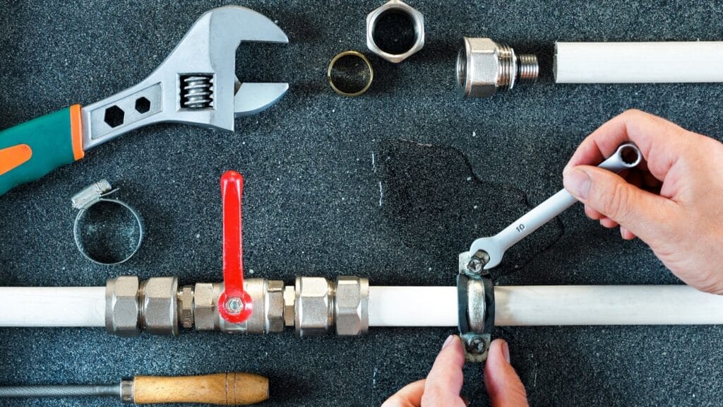Plumber repairing a pipe valve with an adjustable wrench in Colton