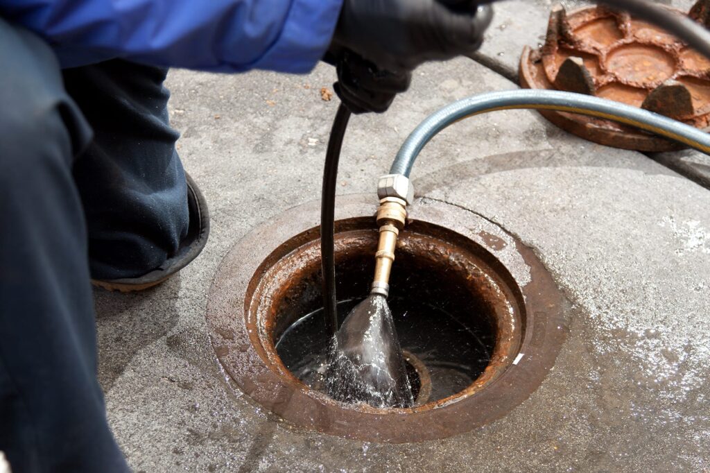 Plumber hydro jetting a sewer line through a manhole in Colton