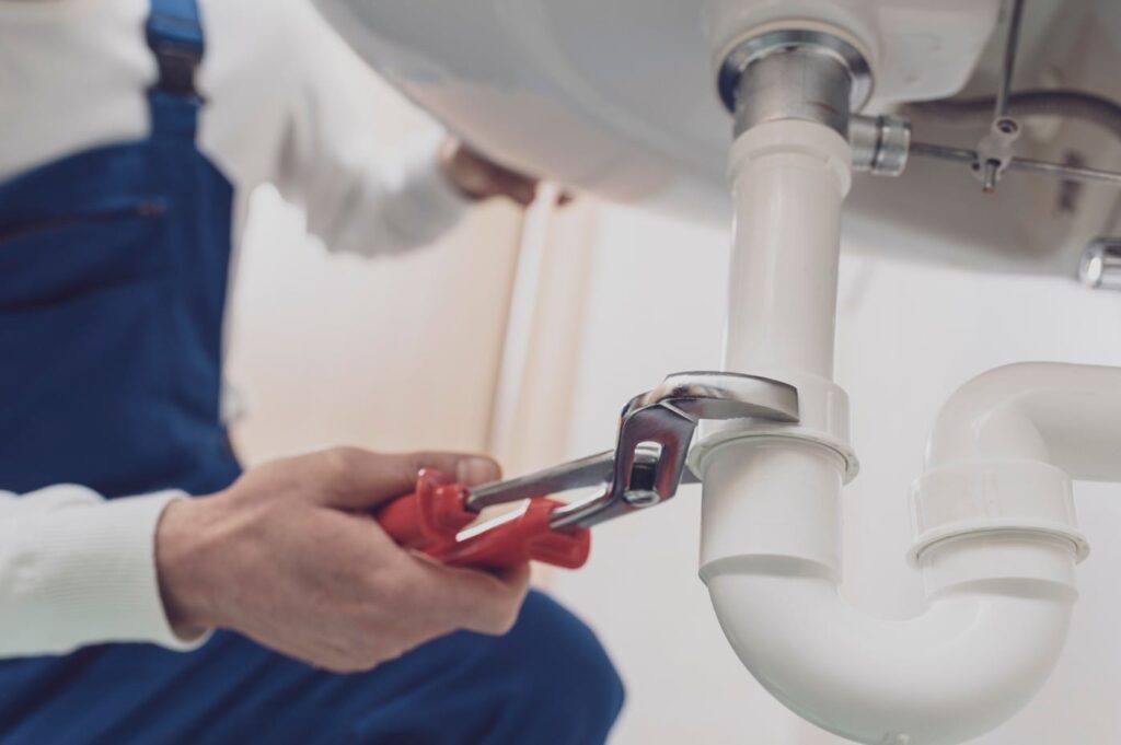 Plumber repairing a white drain pipe beneath a sink in Colton
