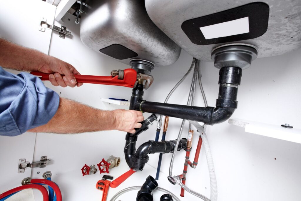 Plumber repairing drain pipes beneath a kitchen sink in Colton