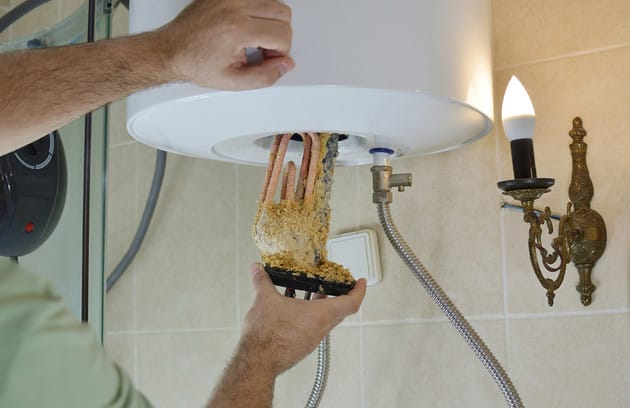 Technician removing mineral buildup from a water heater in Colton